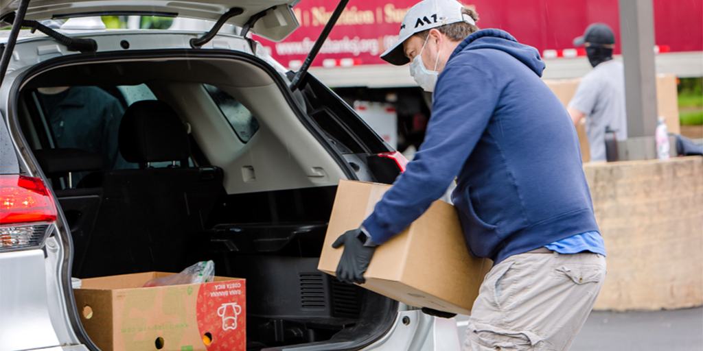 man putting box of food in car