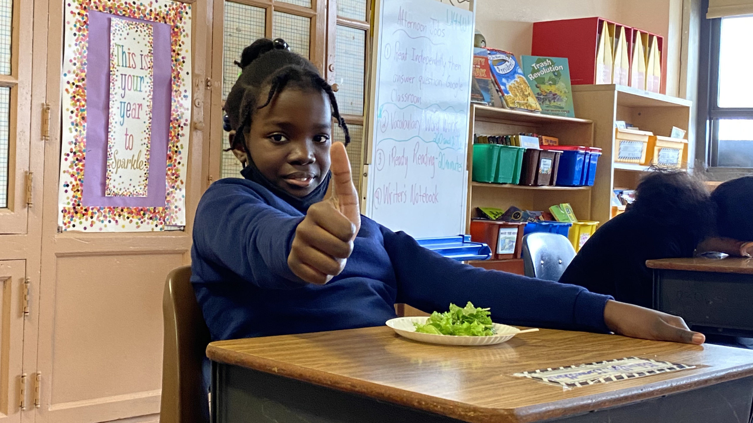 student gives thumbs up at desk with salad