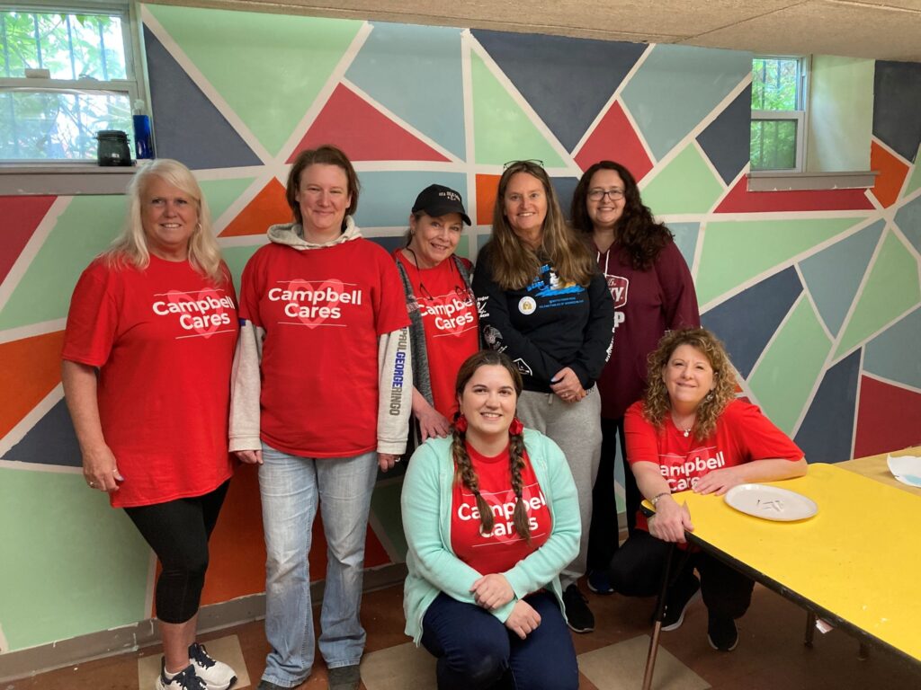 Campbell employees pose in front of mural at Urban Promise